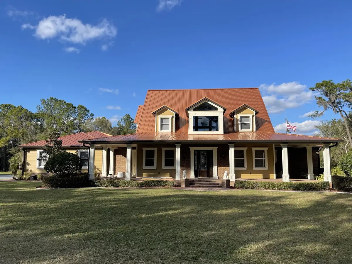 Farmhouse-style home on acreage with a standing-seam metal roof, dormers, and a wraparound porch