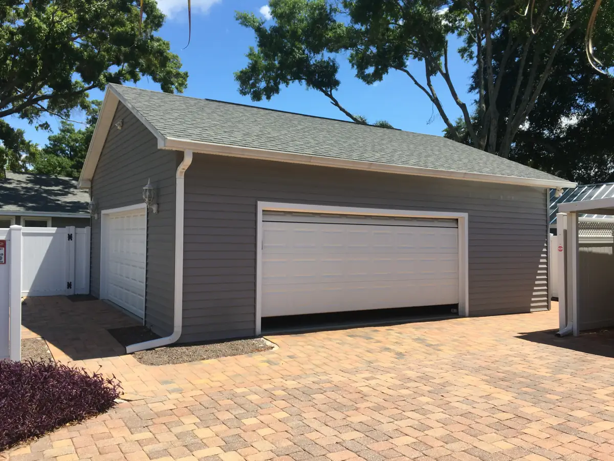 Finished detached garage with its own gable roof, gutters, and a paver drive