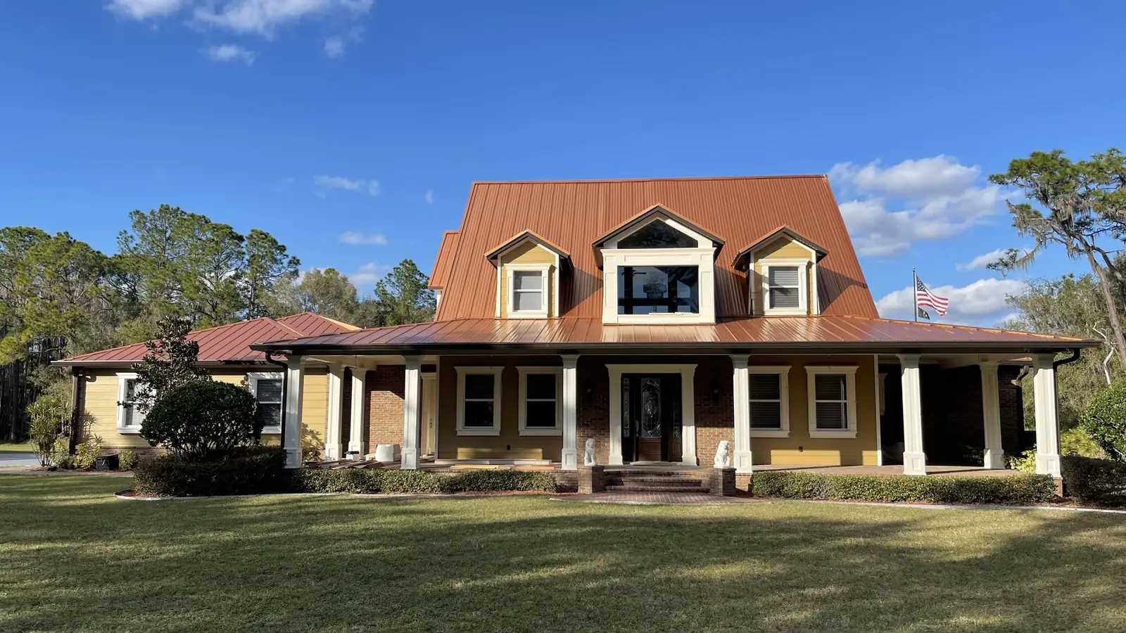 A custom farmhouse-style home on a large open parcel, with a standing-seam metal roof, dormers and a full wraparound porch