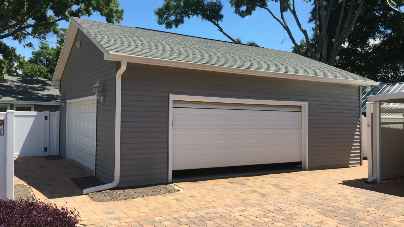 A finished detached accessory building with its own gable roof, gutters and paver drive, set behind the main house