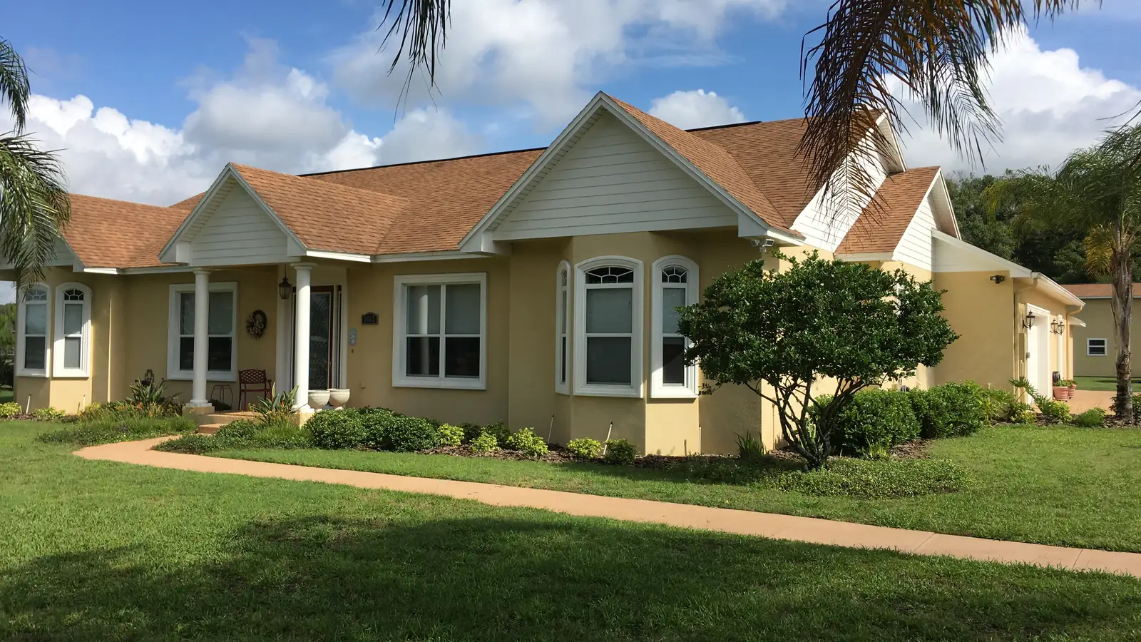 A completed custom home with a tile roof, arched windows and mature palms, finished and landscaped