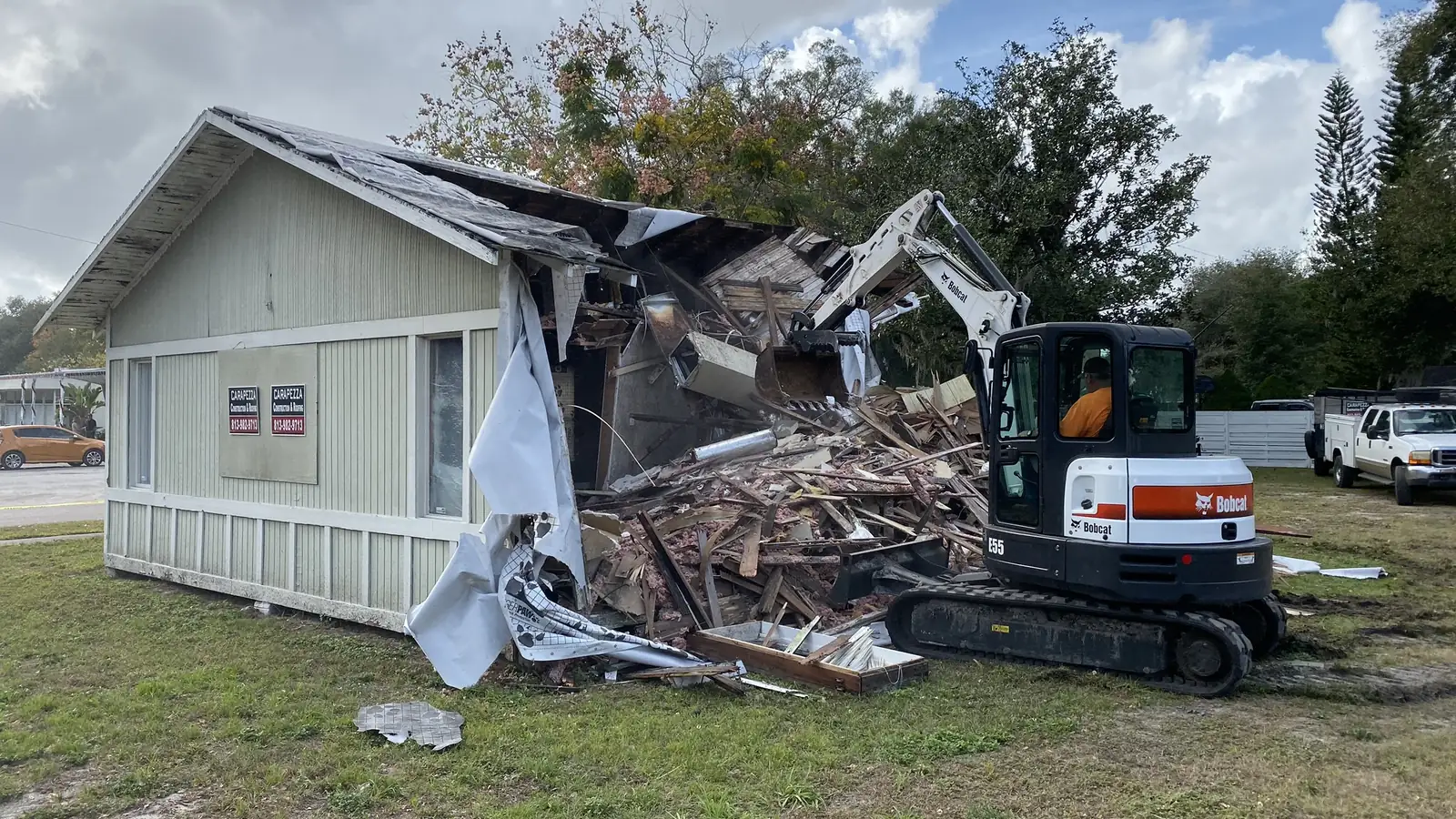 An excavator taking down a single-story coastal cottage, the wall opened up and debris stacked on the lot